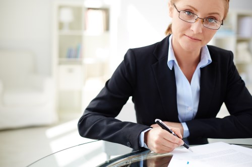 Young businesswoman signing contract and looking at camera in office